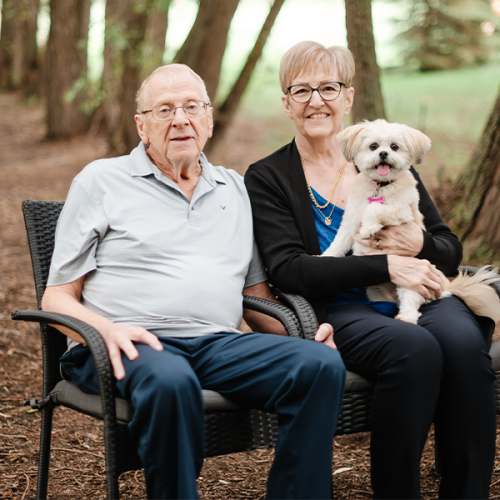A photo of Terry and Judy sitting on a park bench with their dog on Judy's lap.
