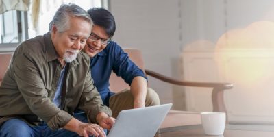 A picture of an adult man and his senior father working on a laptop together.